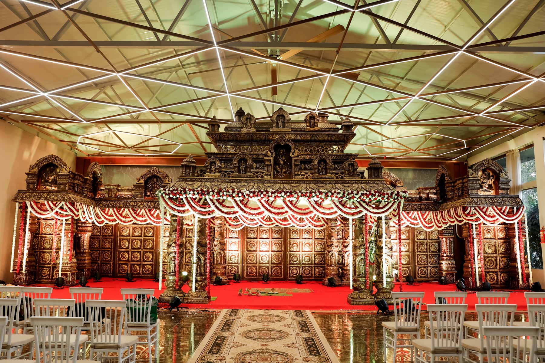 Ornate carved wedding mandap with red and gold drapery by SGR Decorators